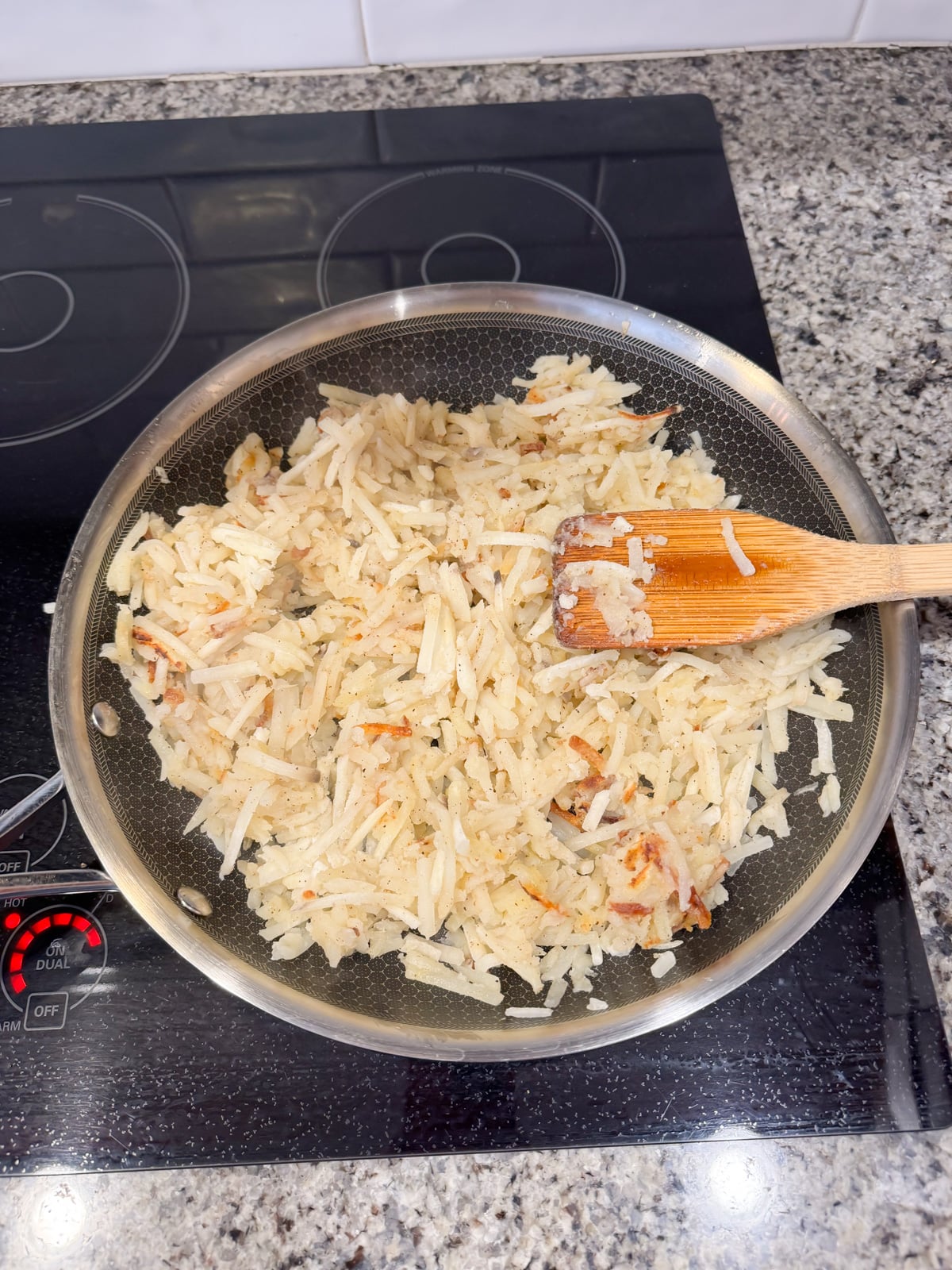 cooking shredded hash browns in a skillet with a wooden spoon.