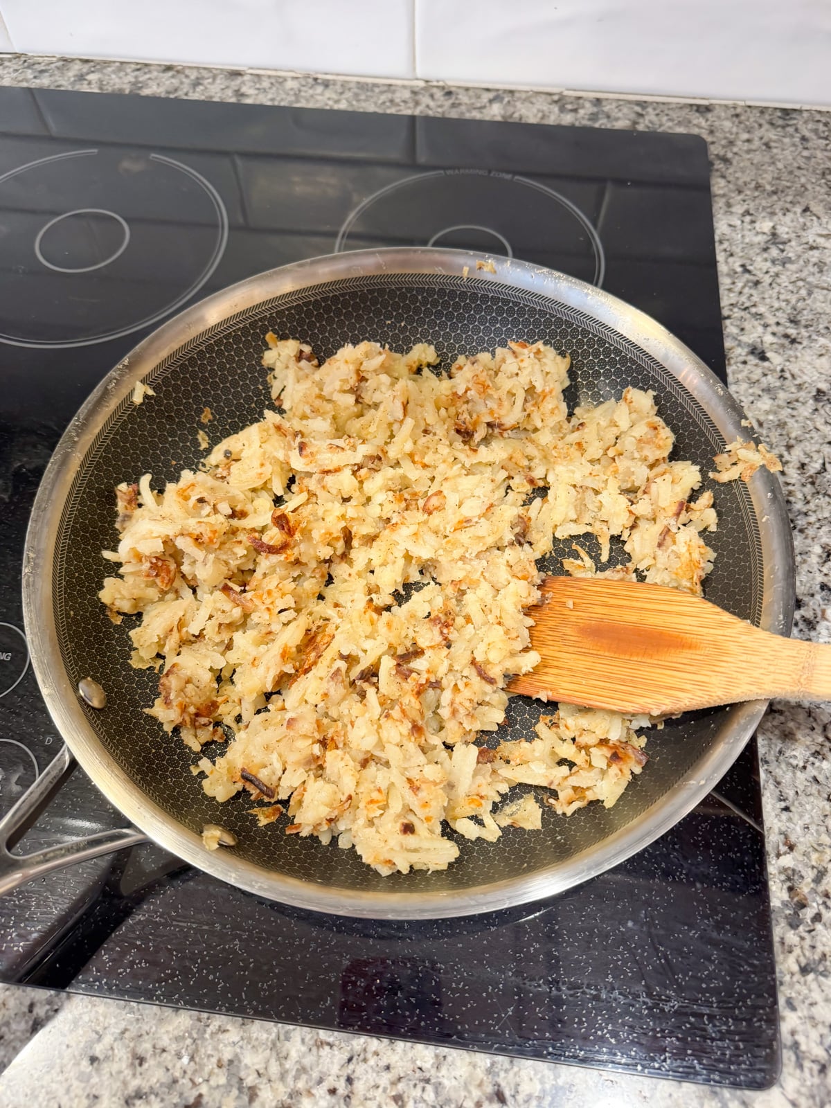 Crisping up hash browns in a skillet on the stove with a wooden spoon.