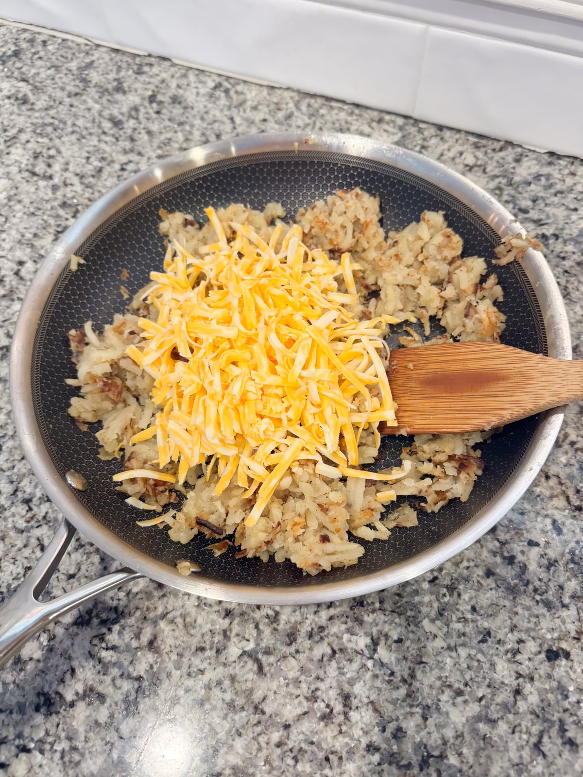 Adding shredded cheese to cooked hash browns in a skillet.