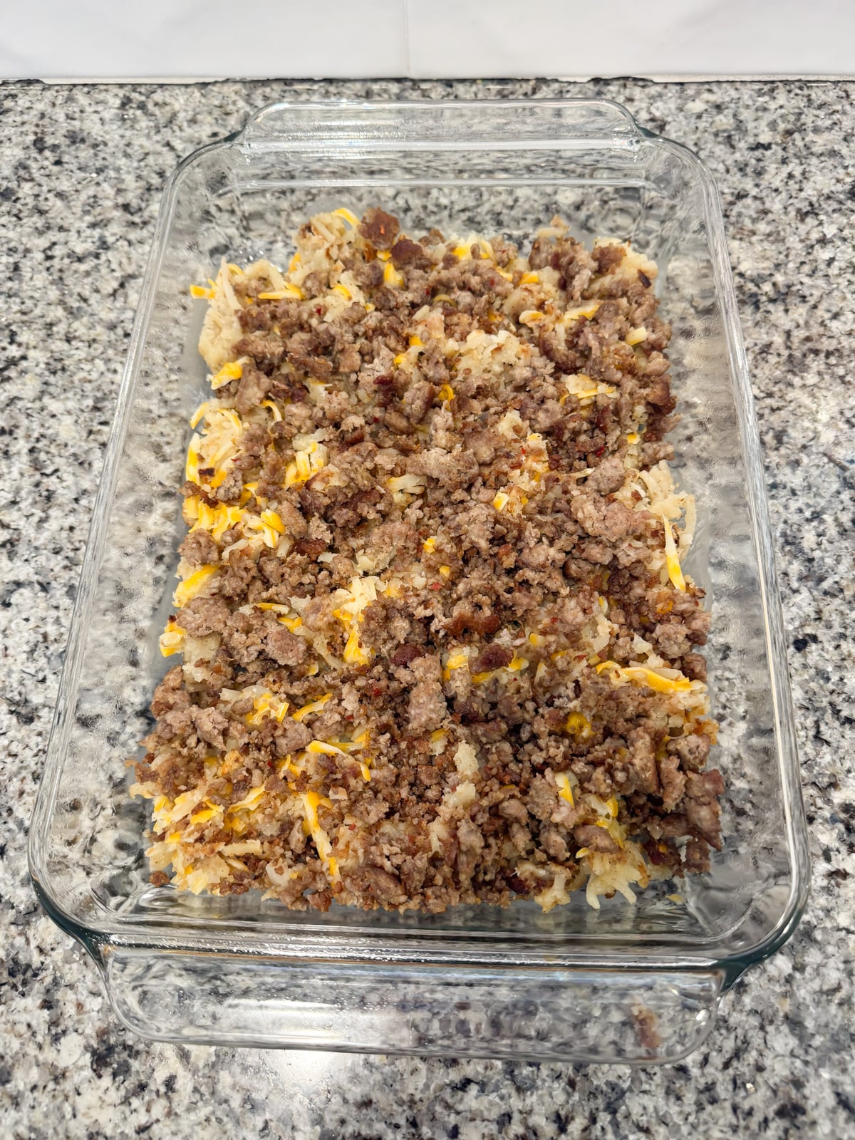 An even layer of sausage spread on top of cooked hashbowns in a baking pan.