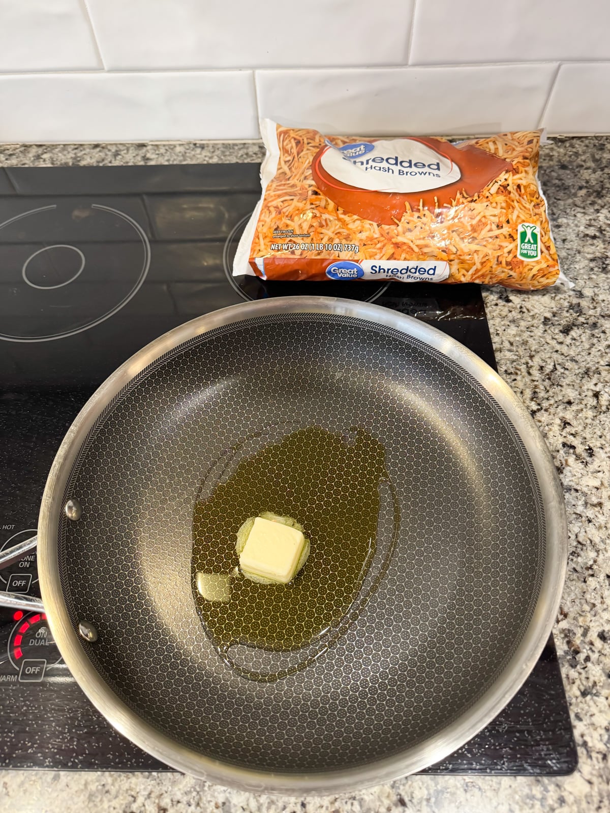 butter and olive oil in a large skillet with a bag of shredded hash browns in the back.