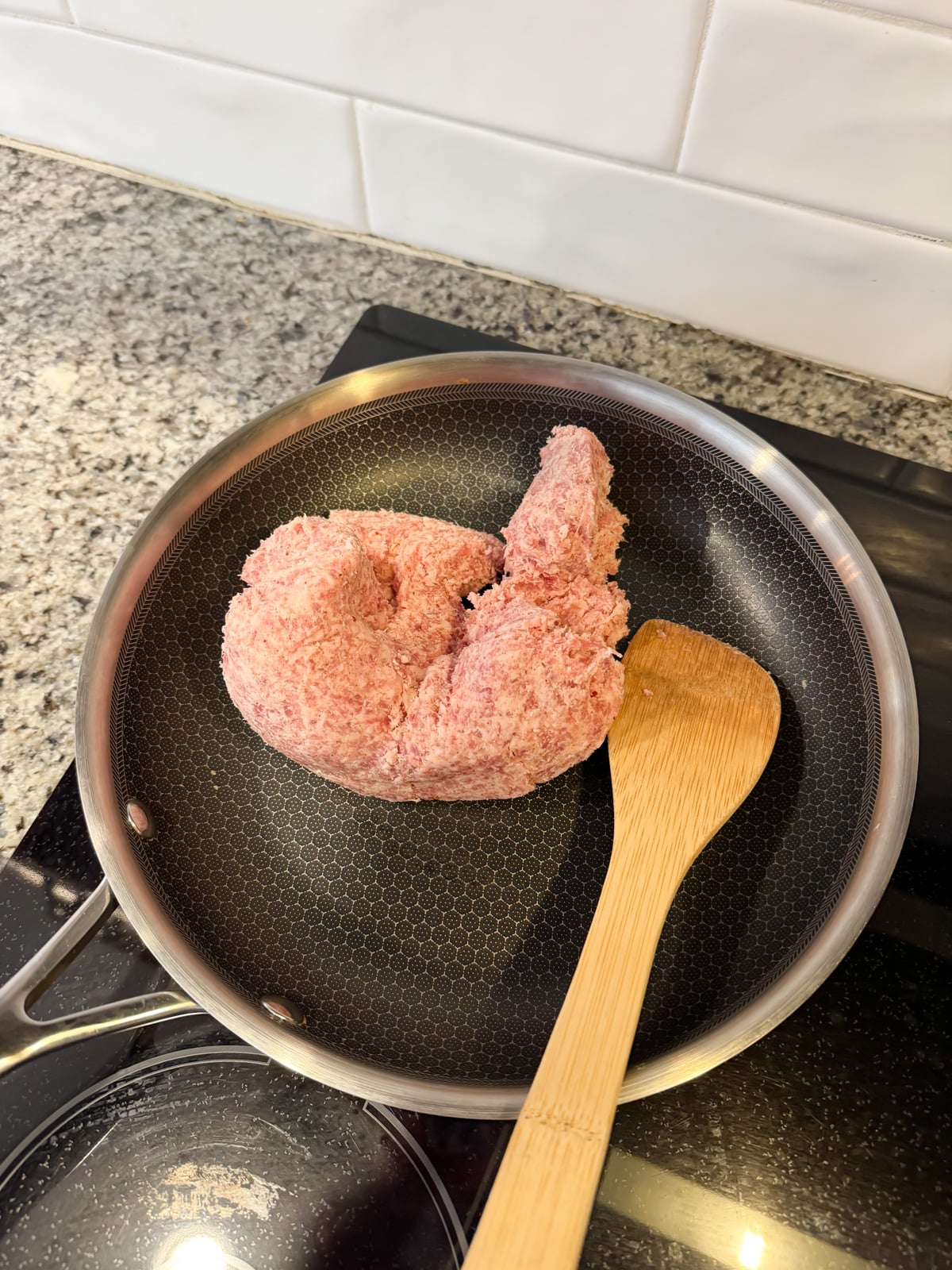 Sausage and a wooden spoon in a large skillet on the stove.