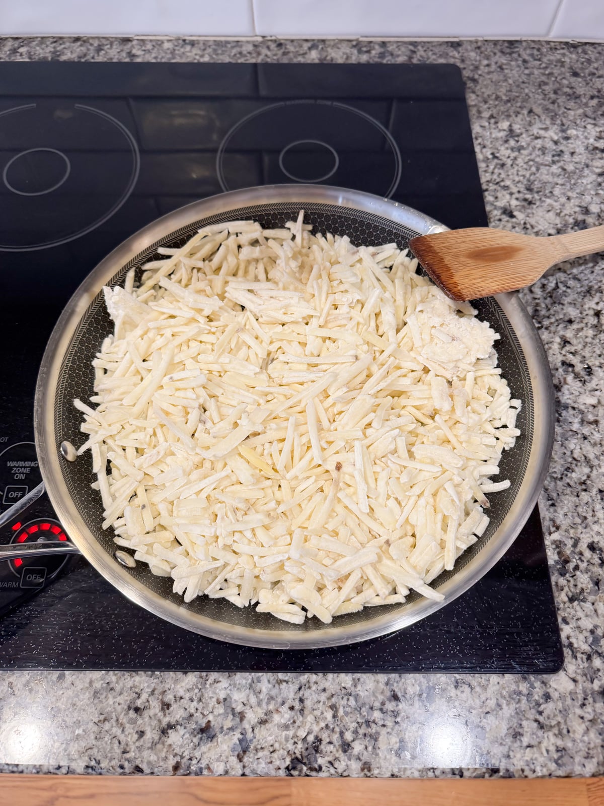 cooking shredded hash browns in a skillet with a wooden spoon.
