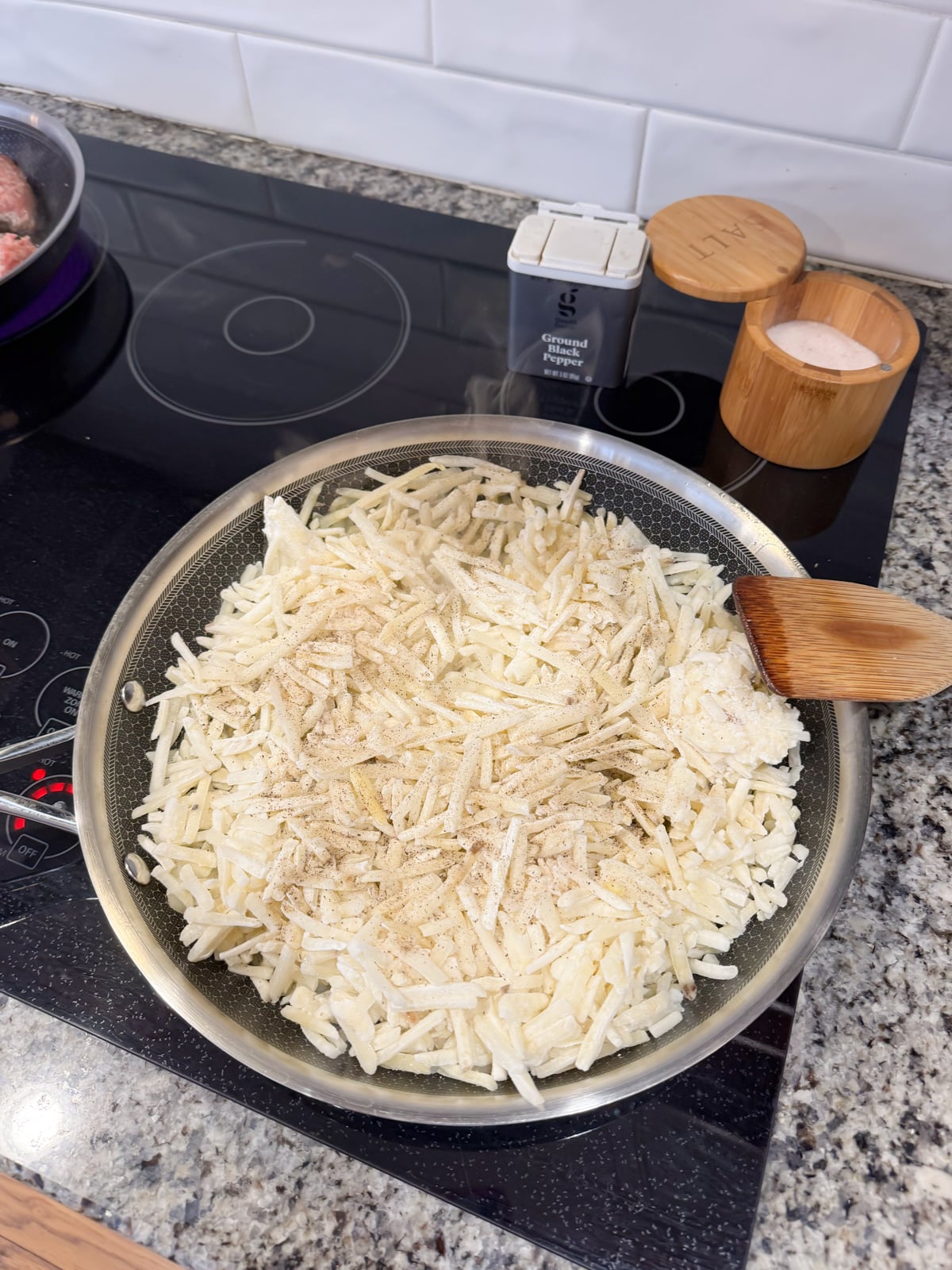 Seasoning hash browns cooking in a skillet with salt and pepper.